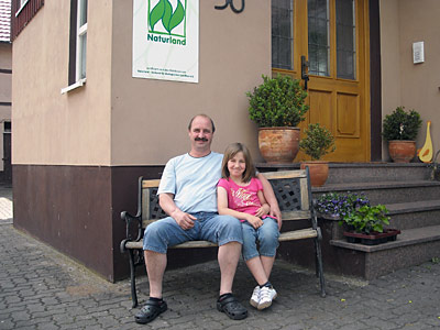 © Bio mit Gesicht Betriebsleiter mit Kind vor Wohnhaus