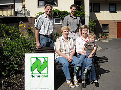 Betriebsleiterehepaare Senior und Junior mit Kleinkind neben Naturland Schild