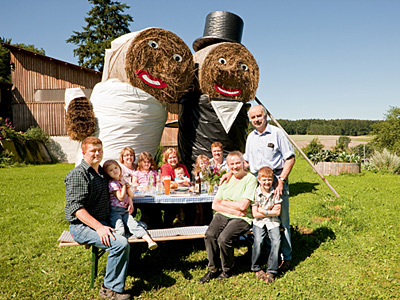 © Feneberg/Bio mit Gesicht Betriebsleiter mit Familie und Eltern vor überlebensgroßen Figuren aus Strohballen
